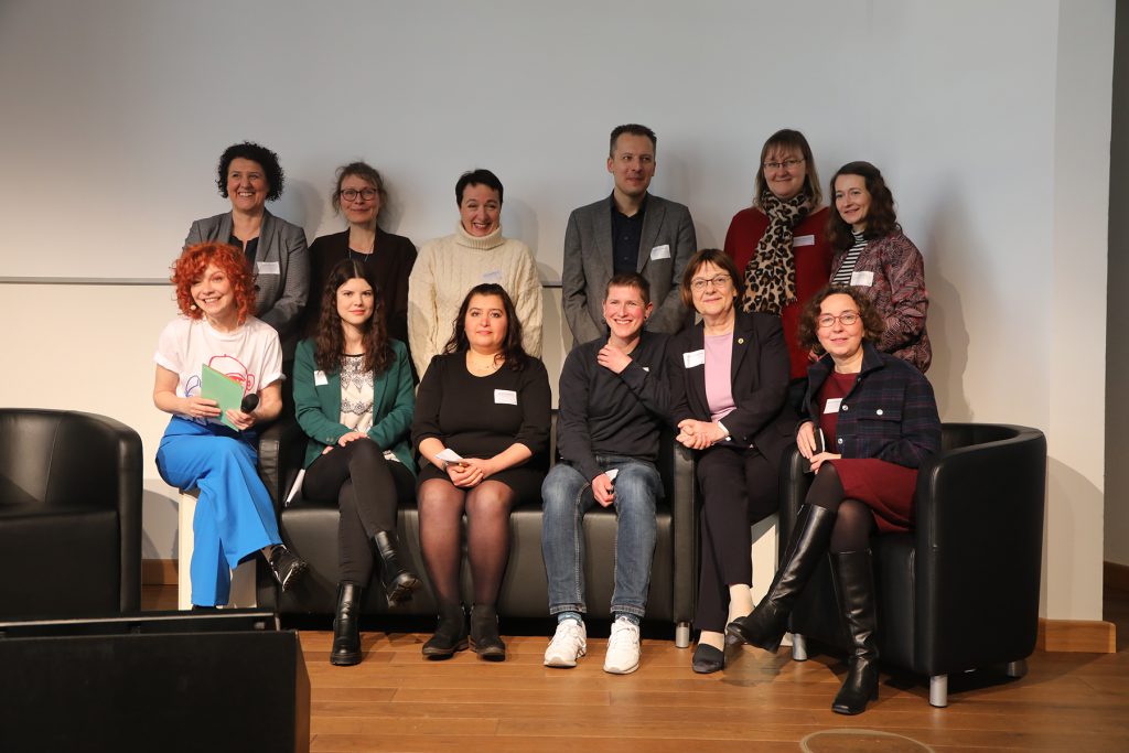 Gruppenbild der Grußwortredner*innen, der Moderatorin und der Brandenburger*innen, die ihre Geschichten auf dem Podium erzählten